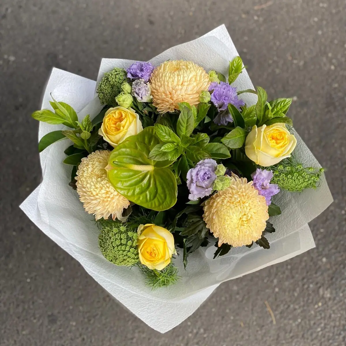 Hand-tied bouquet of yellow roses, champagne disbuds and lilac lisianthus in white wrap