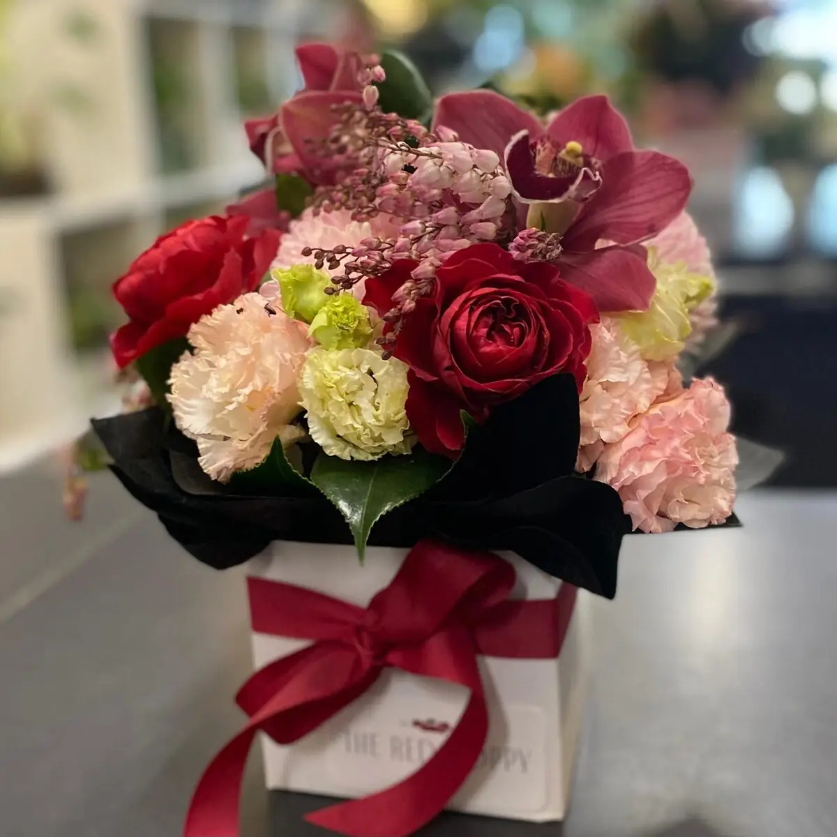 Petite boxed arrangement of red and pink blooms with orchids
