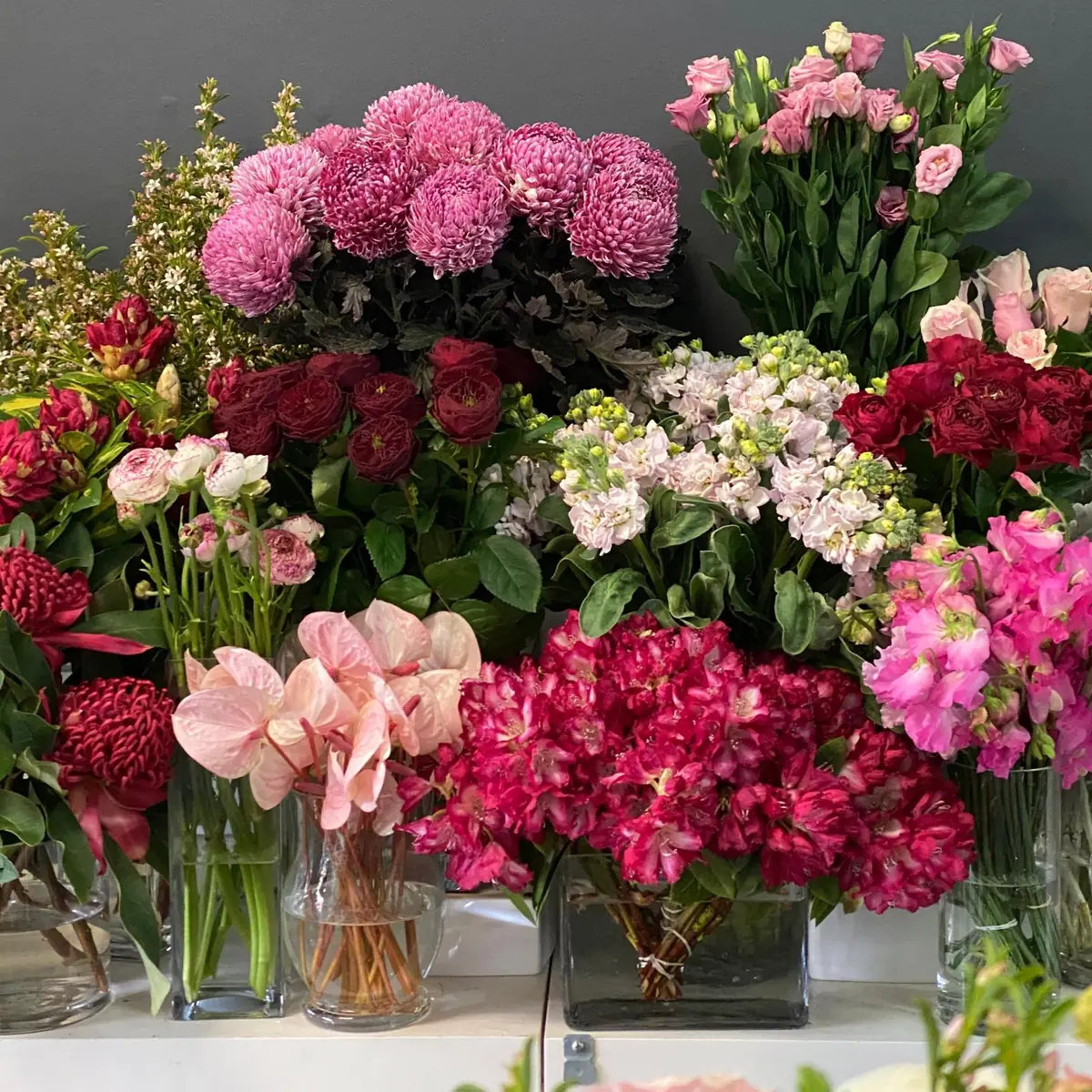 Vases of fresh-cut flowers massed on the shop's flower stand: chrysanthemums, ranunculus and sweet peas in pinks and reds
