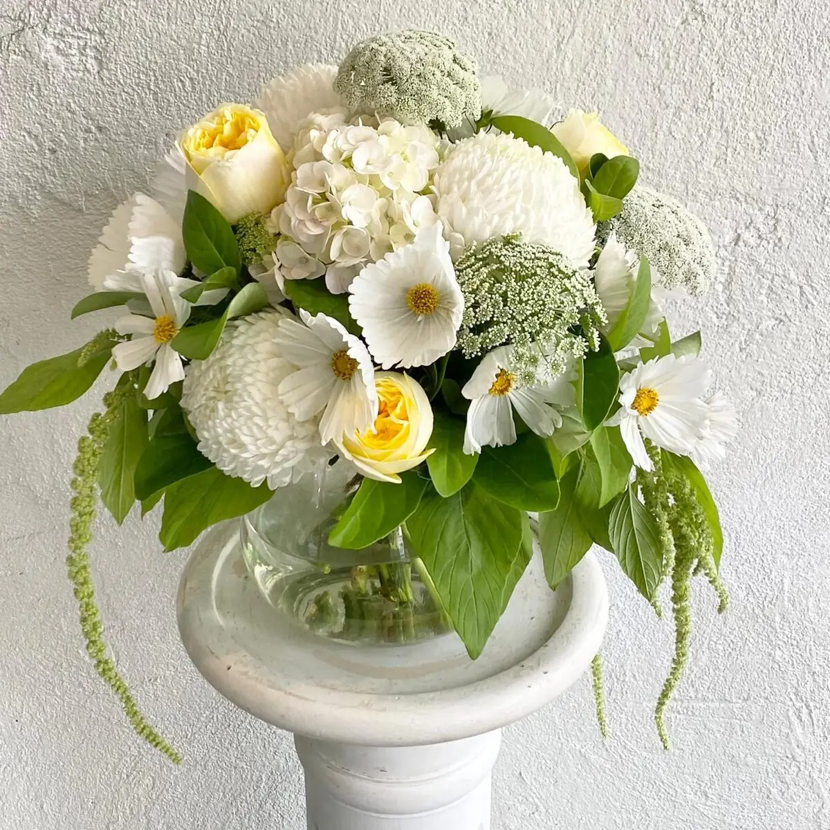 White hydrangea, chrysanthemum and cosmos with soft yellow roses in a clear glass vase