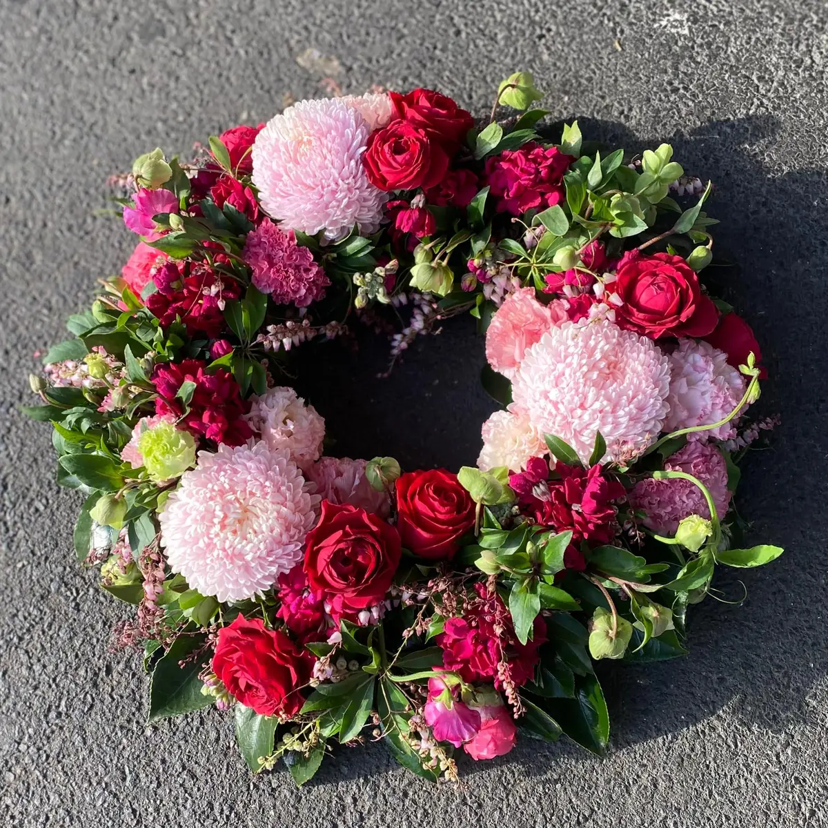 A sympathy wreath of red roses, blush chrysanthemums and carnations