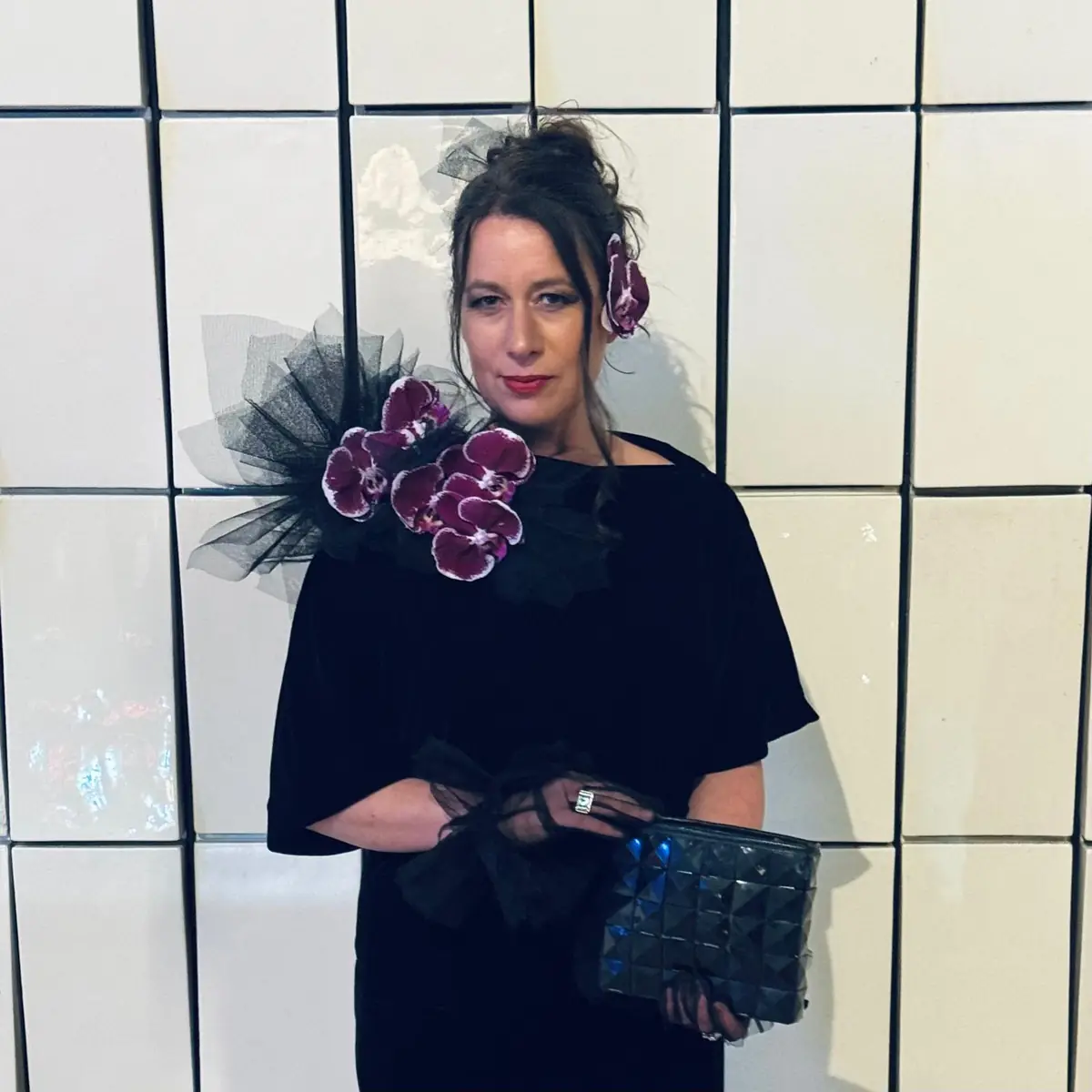 Zoe McMahon in black velvet with an orchid corsage, against a white-tiled wall